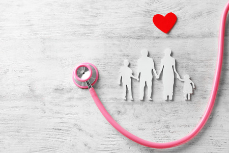 Family figure, red heart and stethoscope on wooden background. Health care concept