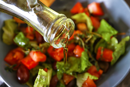 Pouring of olive oil into bowl with fresh vegetable salad, closeup