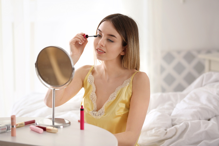 Beautiful young woman applying makeup in morningの写真素材