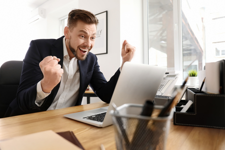 Happy excited businessman with laptop in officeの写真素材