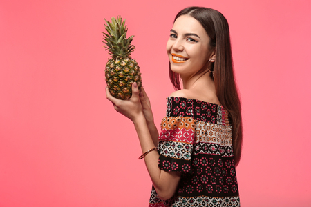 Attractive young woman with pineapple on color backgroundの写真素材
