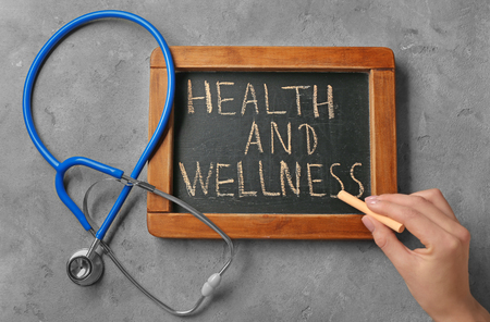 Woman writing phrase "Health and wellness" on blackboardの写真素材