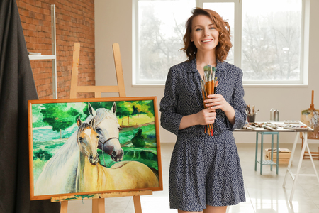Female artist with brushes near beautiful picture in workshopの写真素材