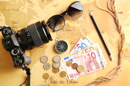 Photo camera, compass, sunglasses and money on world map. Travel planning concept