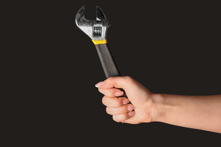 Hand of female car mechanic with adjustable wrench on black background