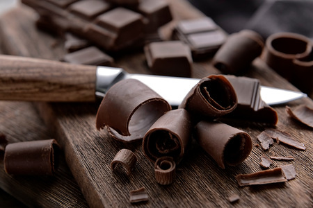 Knife with chocolate curls on wooden board