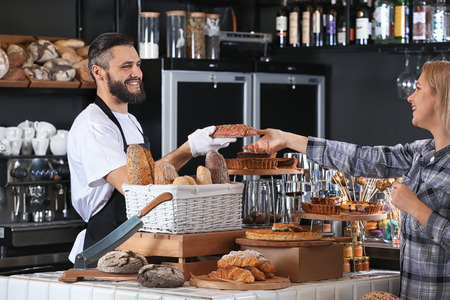 Young man giving fresh bread to woman in bakeryの写真素材