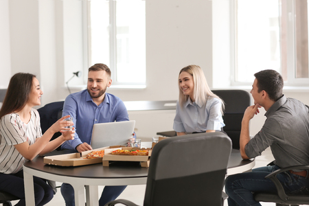 Young people eating pizza at table in officeの写真素材
