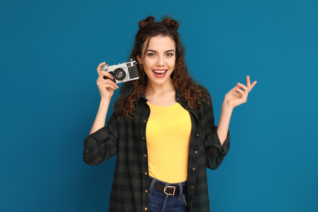Portrait of beautiful young woman with camera on color backgroundの写真素材