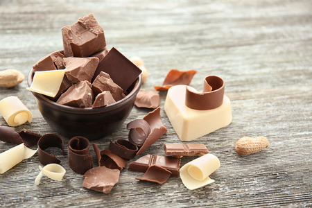 Bowl with pieces of chocolate and curls on wooden table