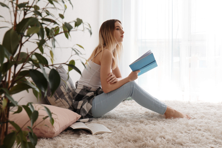 Young woman reading book on floor at homeの写真素材
