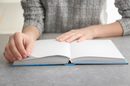 Young woman reading book at table, closeup