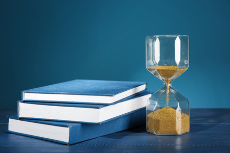Hourglass with books on table against color background. Time management conceptの写真素材