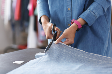 Young female tailor cutting fabric in atelier