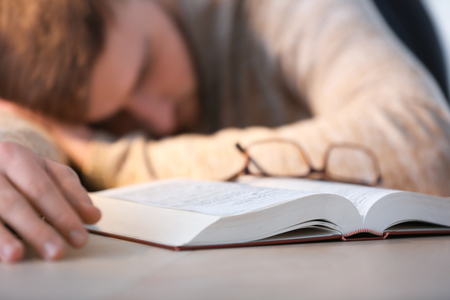 Tired young man sleeping at table with bookの写真素材