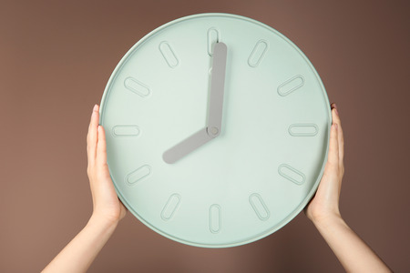 Female hands holding clock on color background. Time management concept