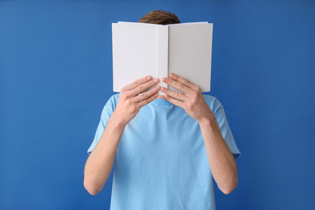 Young man reading book on color background