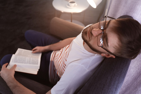 Young man with book sleeping in armchair at homeの写真素材
