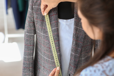 Young female tailor taking measurements of jacket in atelierの写真素材
