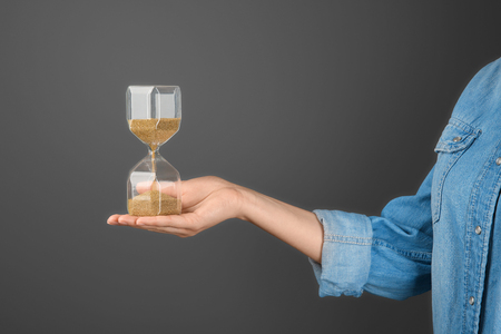 Woman holding hourglass on grey background. Time management concept