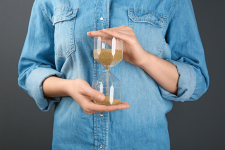 Woman holding hourglass on grey background. Time management concept