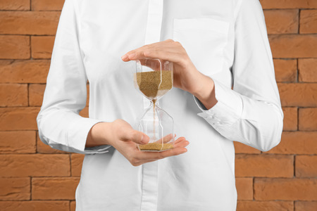 Woman holding hourglass near brick wall. Time management concept