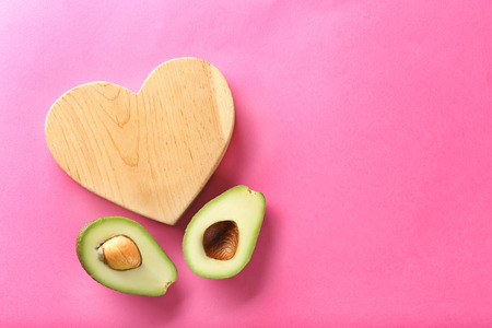Halves of ripe avocado with wooden heart on color backgroundの写真素材