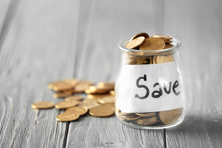 Coins in glass jar with text SAVE on table. Concept of savingsの写真素材
