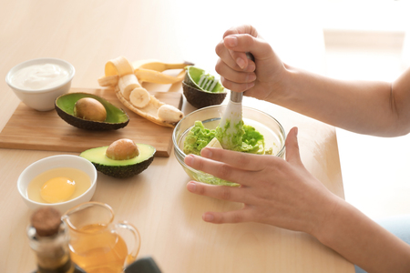 Woman making nourishing mask with avocado in kitchenの写真素材