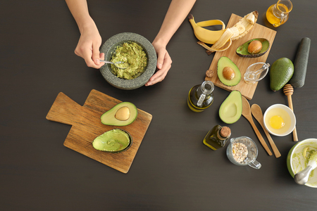 Woman making nourishing mask with avocado in kitchenの写真素材