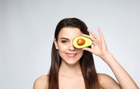 Beautiful young woman with avocado on light backgroundの写真素材