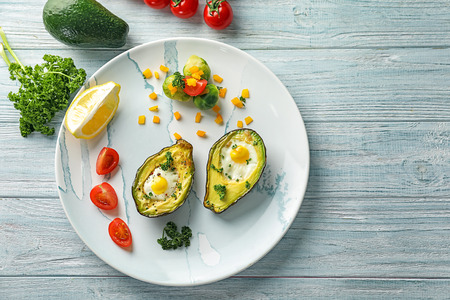 Baked avocado with eggs and vegetables on white wooden backgroundの写真素材