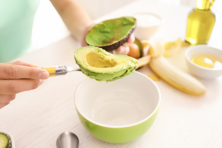 Woman making nourishing mask with avocado in kitchenの写真素材