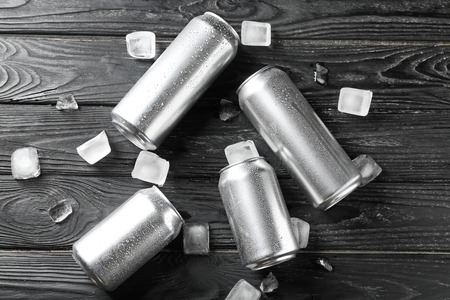 Fresh beer in aluminum cans with ice cubes on wooden background