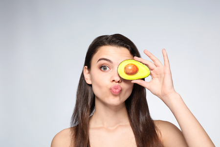 Beautiful young woman with avocado on light backgroundの写真素材