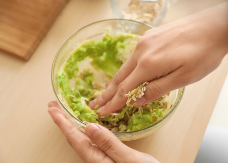 Woman making nourishing mask with avocado in kitchenの写真素材