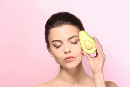 Beautiful young woman with avocado on color background