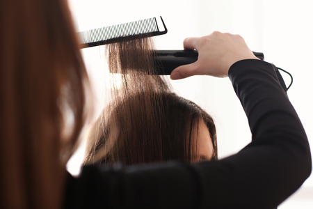 Professional hairdresser straightening client's hair in salonの写真素材