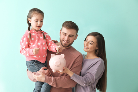 Happy young family with piggy bank on color backgroundの写真素材