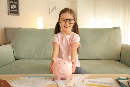 Happy little girl with piggy bank sitting on sofa indoors. Money savings conceptの写真素材