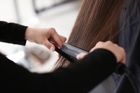 Professional hairdresser straightening client's hair in salonの写真素材