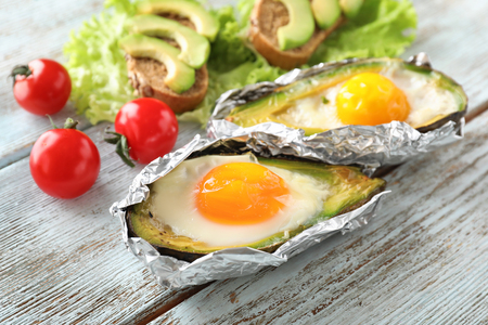 Baked avocado with eggs and vegetables on wooden backgroundの写真素材