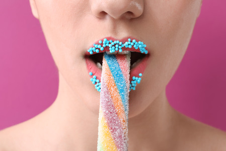 Beautiful young woman with creative makeup and candy on color background, closeupの写真素材