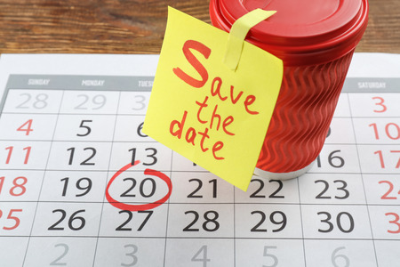Cup, sheet of paper with text "Save the Date" and calendar on wooden tableの写真素材