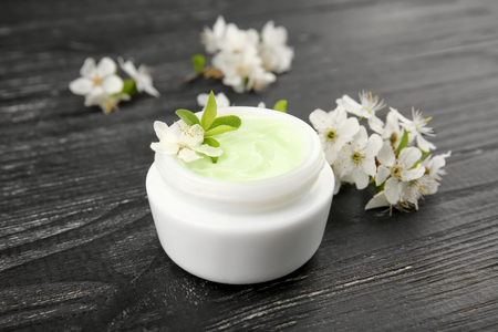 Jar of cream and blooming flowers on dark wooden backgroundの写真素材