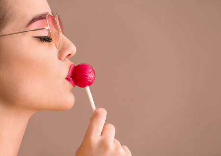 Attractive young woman with lollipop on color background, closeup