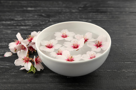 Bowl with water and blooming flowers on dark wooden backgroundの写真素材