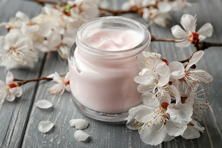 Jar of cream and blooming flowers on wooden backgroundの写真素材