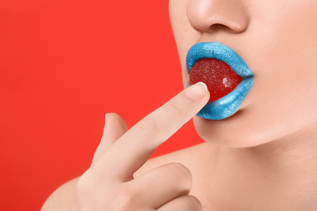 Beautiful young woman with creative makeup and candy in mouth on color background, closeupの写真素材