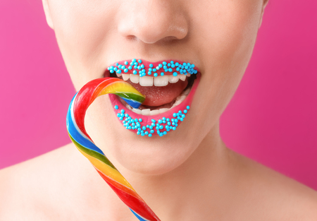 Beautiful young woman with creative makeup and candy cane on color background, closeupの写真素材